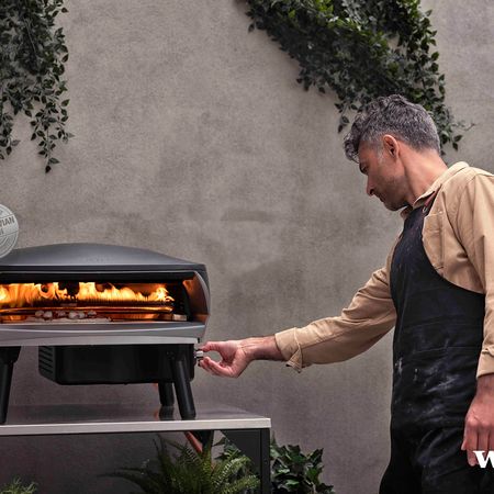 Ein Mann steht vor einem Grill und schaut nach einer Pizza
